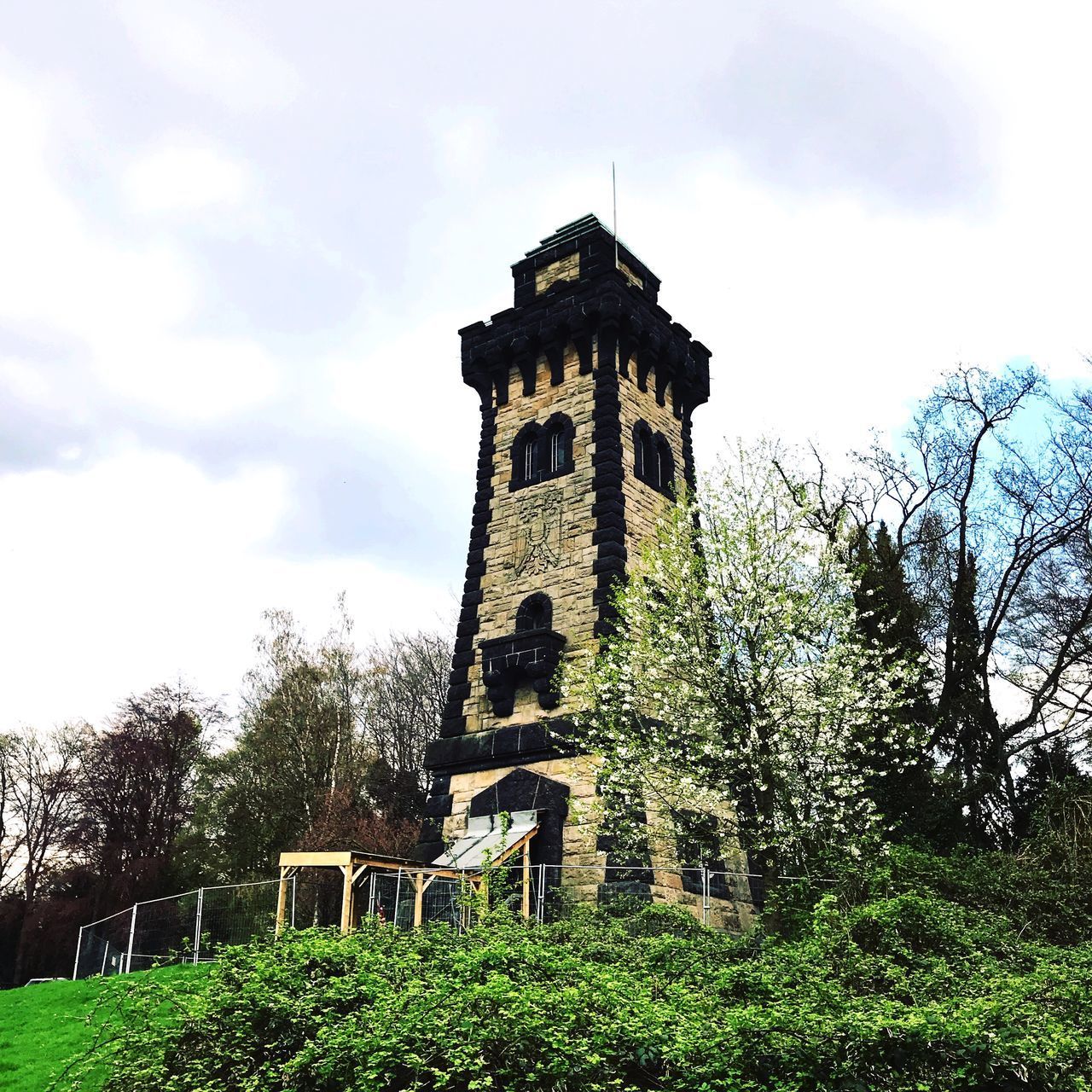 LOW ANGLE VIEW OF OLD TOWER AMIDST TREES AND BUILDING AGAINST SKY