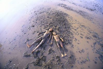 High angle view of boys lying in muddy water