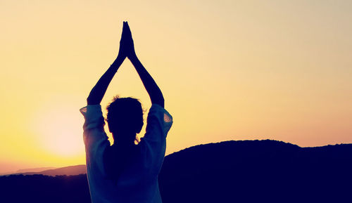 Practicing yoga at sunset, woman figure in backlight, mountains in the background.