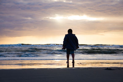 Rear view of man standing on beach during sunset