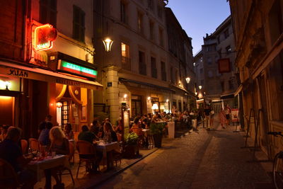 People on street amidst illuminated buildings at night