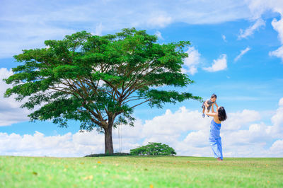 Woman standing by tree on field against sky