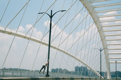 Man levitating on arch bridge against cloudy sky