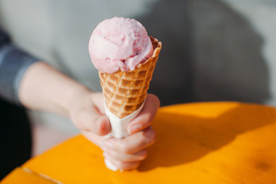 Cropped image of woman sitting by table and holding ice cream cone in hand 