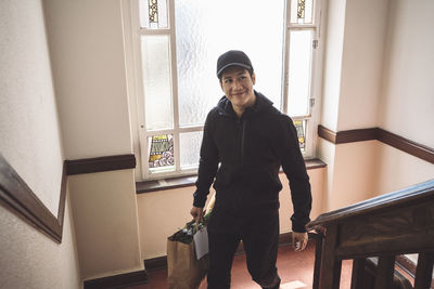 High angle view of smiling delivery man with package climbing staircase