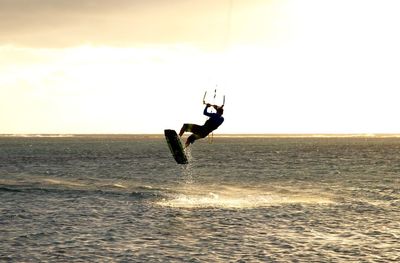 Silhouette man kiteboarding in sea against sky during sunset