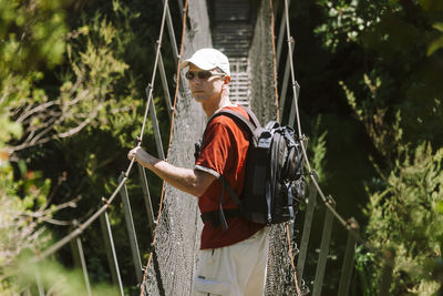 Side view of hiker standing on footbridge in forest