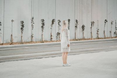 Rear view of woman walking on road against wall