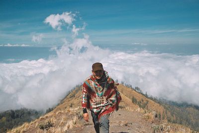 Portrait of young man hiking on mountain against cloudscape