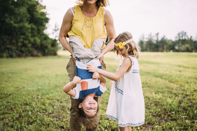 Low section of mother carrying son upside down while standing with daughter at park