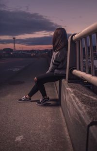 Side view of woman sitting on railing during sunset
