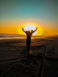 Silhouette woman standing on beach with arms outstretched during sunset