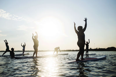Silhouette people exercising on paddleboard in sea against sky