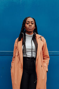 Portrait of young woman wearing overcoat while standing against blue wall