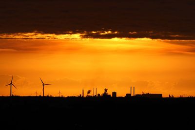 Silhouette of wind turbine against orange sky