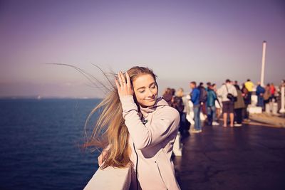 Smiling young woman with blond hair standing against sea at beach