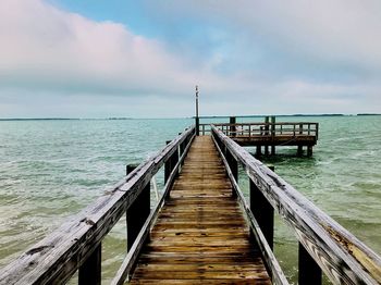 Wooden jetty leading to pier over sea against sky