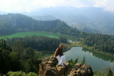 Woman sitting on mountain by mountains with lake background