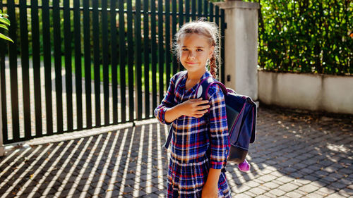 Girl with backpack ready to school and stands with hand on her heart at first day after vacation