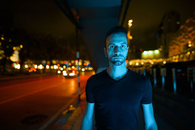 Portrait of young man standing on illuminated street at night