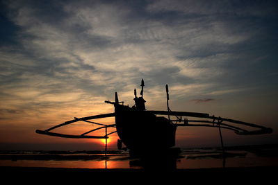 Silhouette outrigger canoe moored at beach during sunset