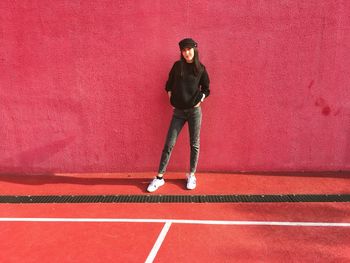 Full length portrait of young man standing against red wall