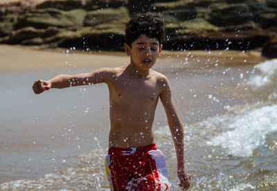 Playful boy splashing sea water at beach