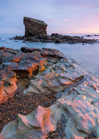 Rock formation on beach against sky during sunset