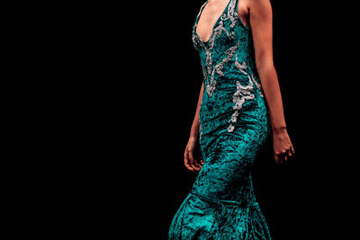 Details of a velvet green evening dress on a female figure on a black background.