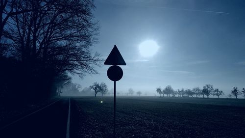 Road sign by trees against sky