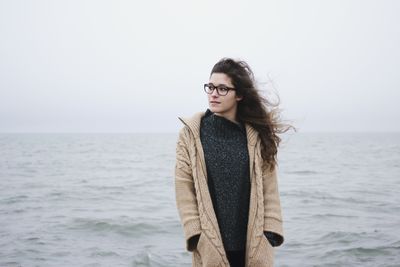 Portrait of young woman standing at seaside against sky