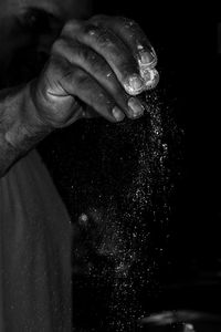 Close-up of man pouring flour against black background