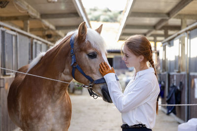 Redhead woman stroking horse at stable