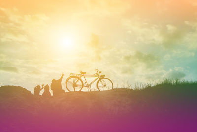 Silhouette people riding bicycle on field against sky during sunset