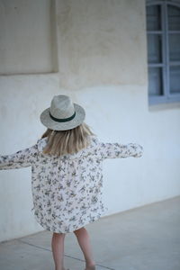 Rear view of woman wearing hat standing against wall