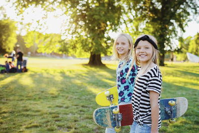 Portrait of smiling friends with skateboards at public park