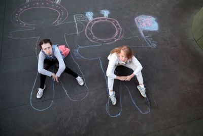 Full length of girls sitting on drawings at street