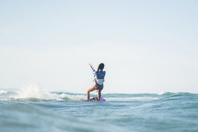 Back view of fit female kite surfer in swimsuit ridding waves in sea on sunny day in summer