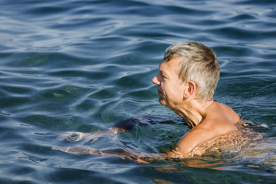 Shirtless man looking away while swimming in sea