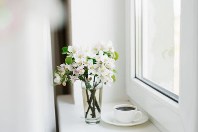 Cup of coffee on a white plate and a vase of flowers on the windowsill. cozy easter, spring 