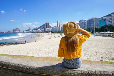 Beautiful young woman sitting on wall enjoying the cityscape of rio de janeiro, brazil