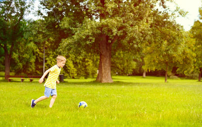 Full length of boy playing on soccer field against trees