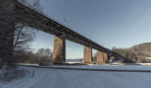 Bridge over snow covered field against sky