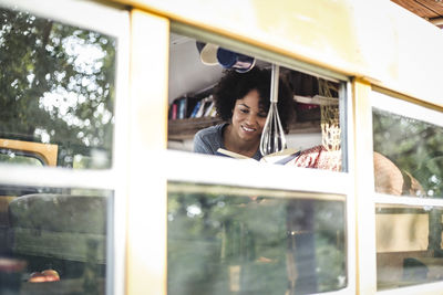 Young afro woman reading book while lying in motor home seen through window