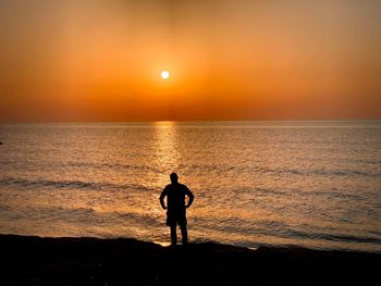 Silhouette man standing on beach against orange sky