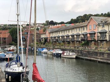 Boats moored in river by buildings against sky