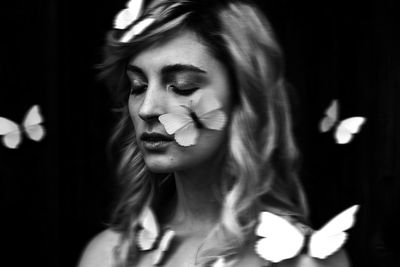 Close-up of young woman with butterflies against black background