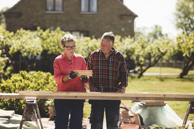 Senior couple examining wooden plank while standing at yard