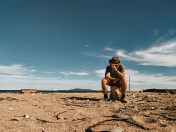 Man sitting on rock against sky