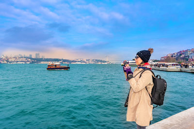 Woman photographing river in city against blue sky